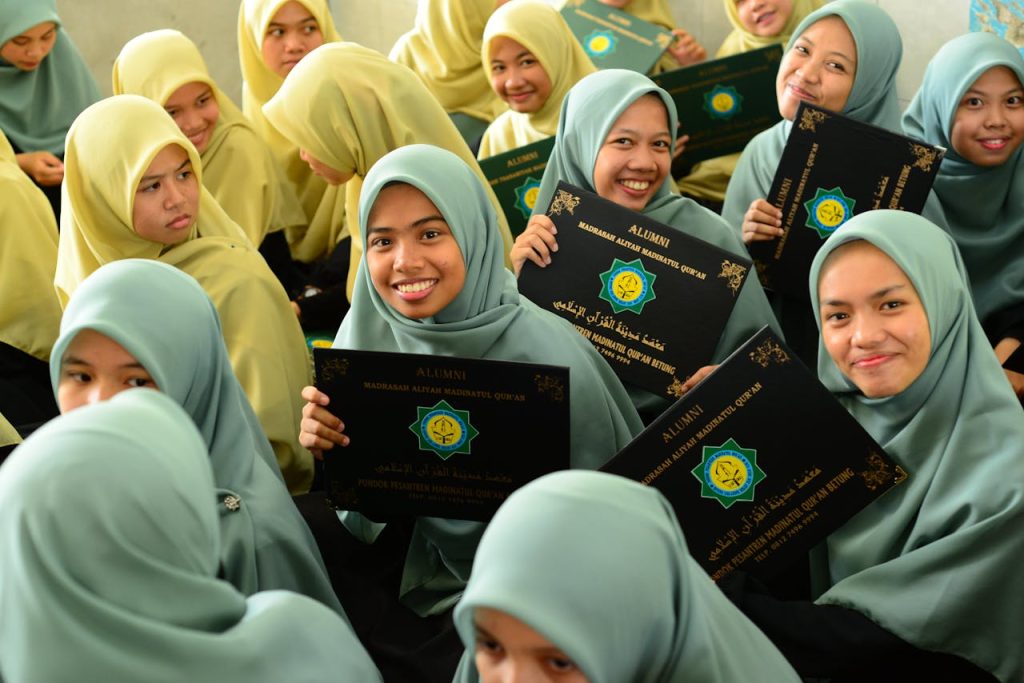 Group of young Muslim students celebrating graduation, holding diplomas with smiles.